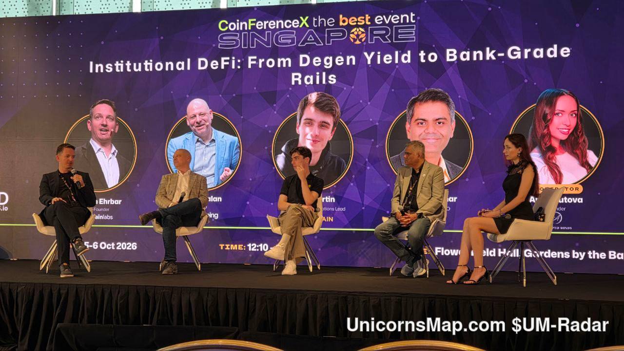 CoinFerenceX The Best Event Singapore 2026 — wide venue-day frame of the Day-2 'Institutional DeFi: From Degen Yield to Bank-Grade Rails' panel on the Main Stage at Flower Field Hall, Gardens by the Bay, with six panellists seated in white chairs and the event's own on-stage screen reading 'CoinFerenceX the best event SINGAPORE', the panel title, '5-6 Oct 2026', 'TIME: 12:10' and 'Flower Field Hall, Gardens by the Bay'