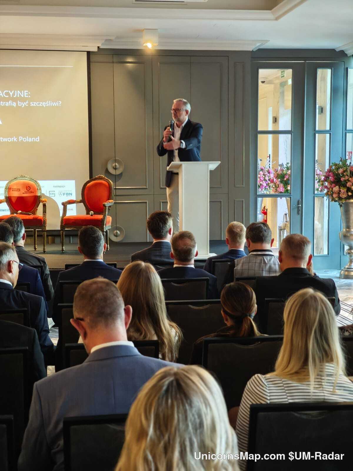 Family Business Forum 2026 — a speaker at the white podium of the Pałac Mała Wieś stage, with the FBN / Network Poland marks on the presentation screen and the seated audience in the foreground