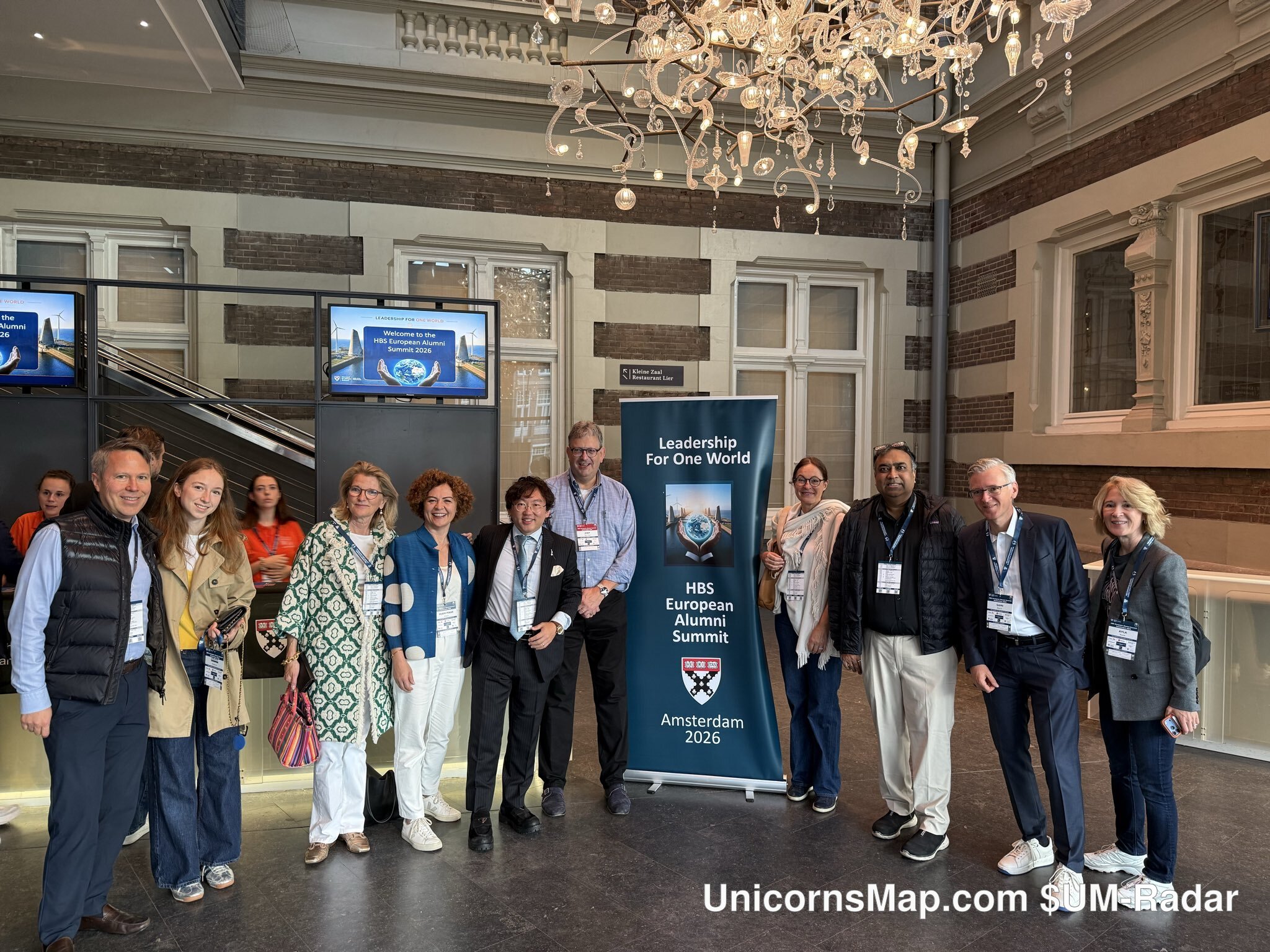 HBS European Alumni Summit 2026 Amsterdam — day-of group photograph with the summit banner: 'Leadership For One World · HBS European Alumni Summit · Amsterdam 2026' and the HBS shield
