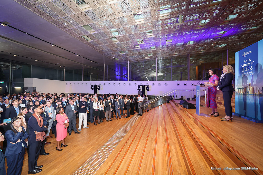 Milken Institute Asia Summit 2026 — Jill Biden at the podium with Ying Staton beside her, standing audience of delegates, under the event's ASIA SUMMIT 2026 backdrop, Four Seasons Hotel Singapore