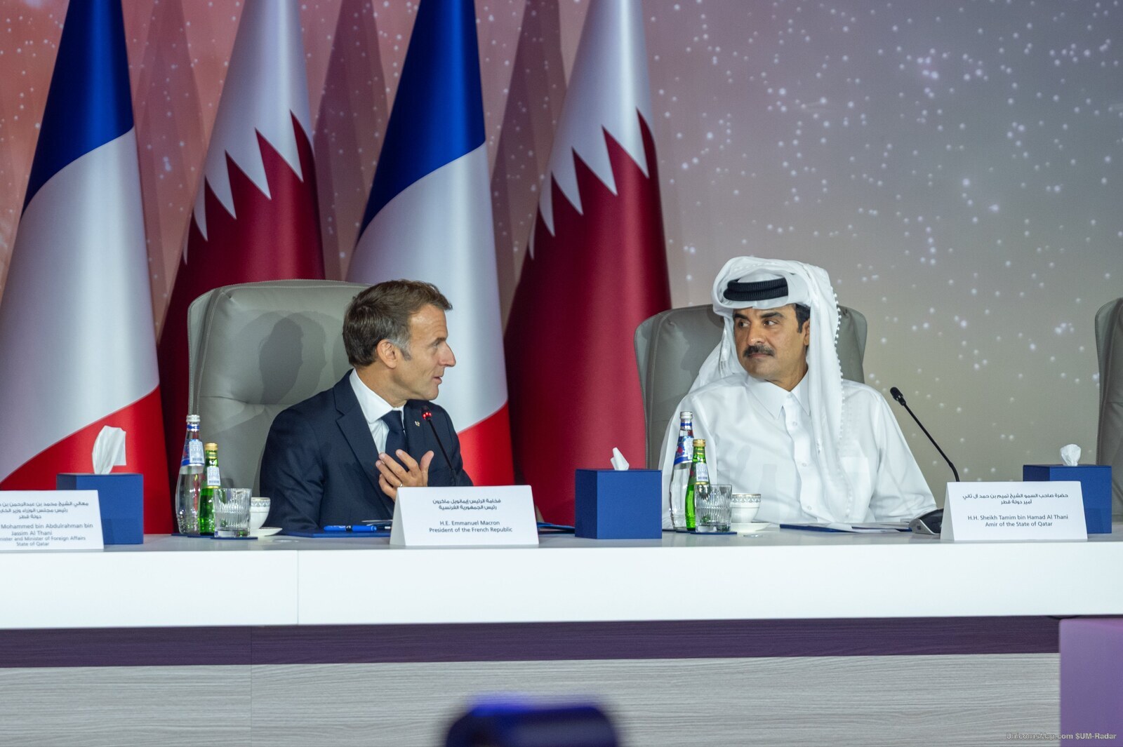 President Emmanuel Macron and HH Sheikh Tamim bin Hamad Al Thani seated side by side at the OPSWF CEO Summit plenary table in Doha, 21 October 2026, with their printed name cards in frame and the French and Qatari flags behind them