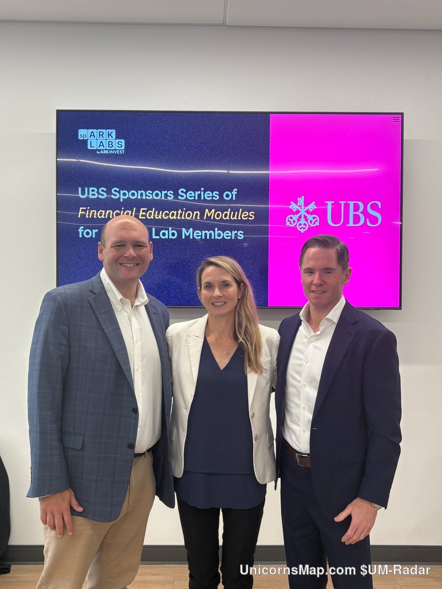 UBS Private Wealth Management Exit Planning Panel at spARK Labs — three adults standing in front of the UBS / spARK LABS screen at the ARK Innovation Center, St. Petersburg: a man in a grey-blue blazer and open-collar shirt, a woman in a cream blazer over a navy top, and a man in a navy blazer and white shirt