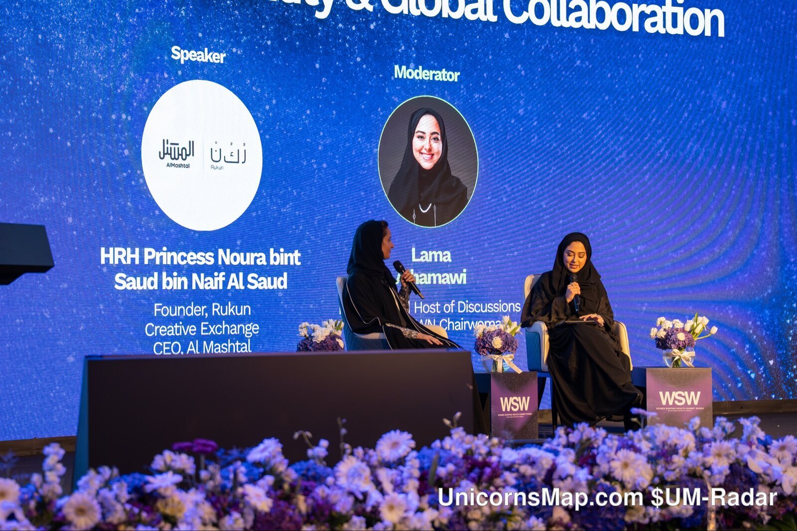 Women Shaping Wealth Summit 2026, Riyadh — day-of stage frame: two carded participants seated on the WSW stage in front of the summit's own on-stage slide, which carries the name cards 'HRH Princess Noura bint Saud bin Naif Al Saud — Founder, Rukun Creative Exchange / CEO, Al Mashtal' under 'Speaker' and 'Lama Alhamawi — Host of Discussions Podcast, Chairwoman of SBWN' under 'Moderator', with WSW lecterns and the summit's own branding in frame